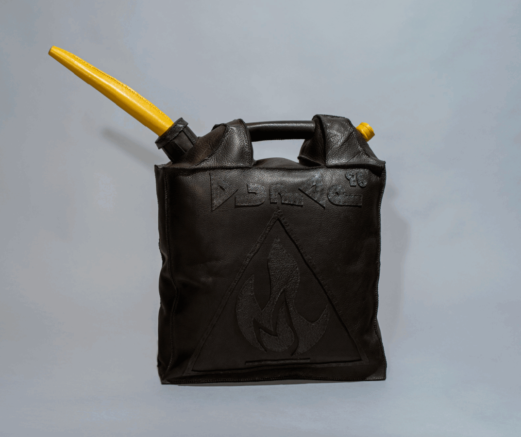 A black leather bag shaped like a fuel canister, with a yellow nozzle attached to a black cap. Embossed symbols and a flame warning sign are visible on the front.